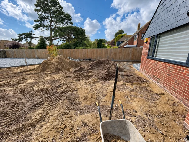 Excavated driveway beside a brick house, with soil piles and a wheelbarrow