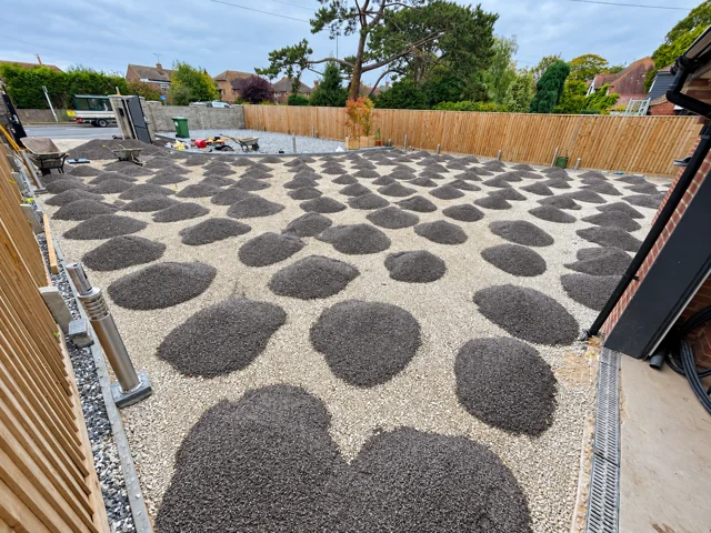Bedding aggregate distributed in small piles across the prepared driveway