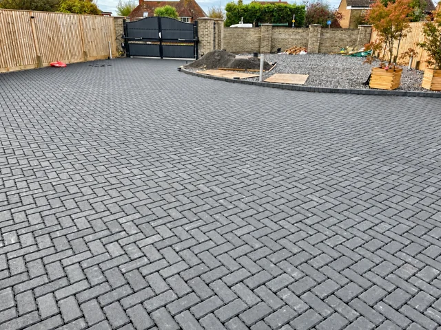 Wide view of the laid grey block driveway with curved edging and entrance gates